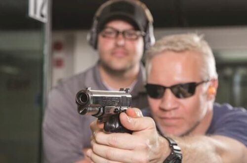 Skytte holder en pistol, mens en instruktør overvåger sikkerheden på banen