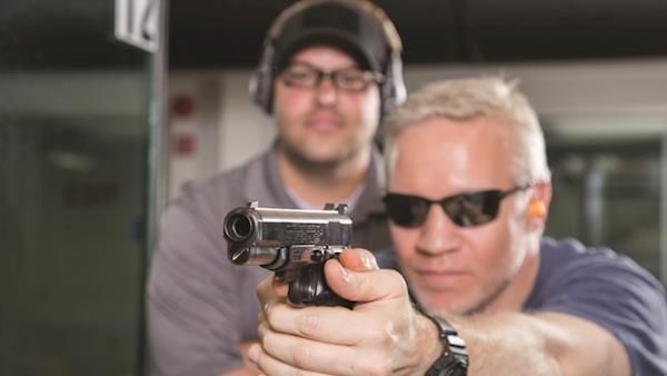 Skytte holder en pistol, mens en instruktør overvåger sikkerheden på banen